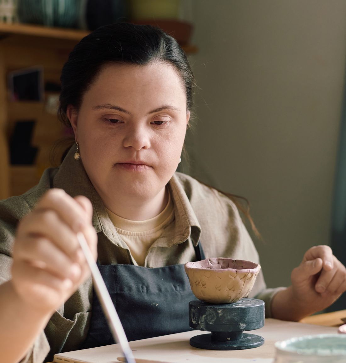 A woman painting a clay bowl at a wooden table, brush in hand