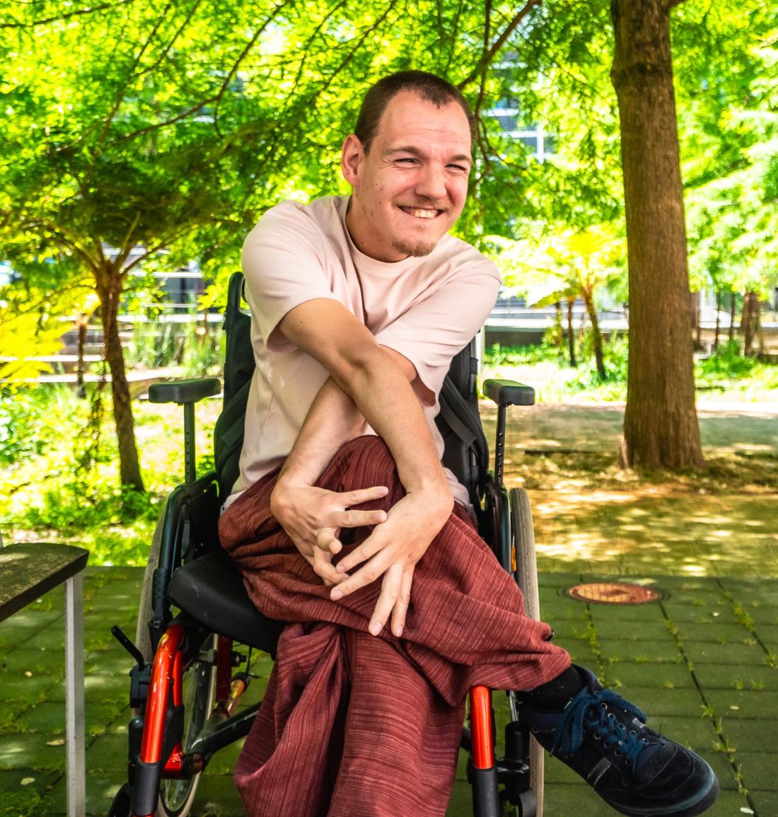 A man in a wheelchair laughing under a leafy tree in a park