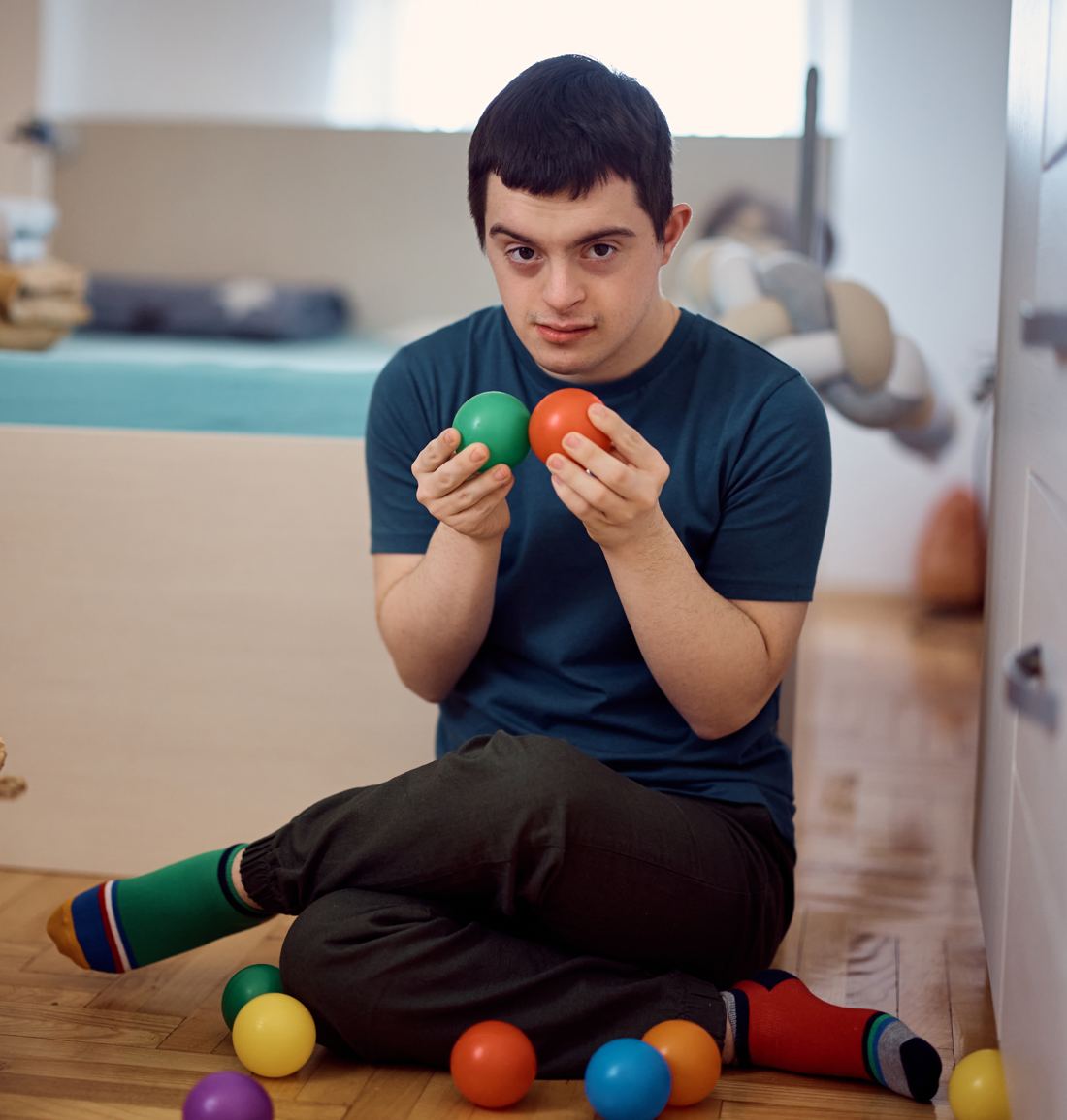 A young man sitting on his bedroom floor sorting coloured balls into a basket